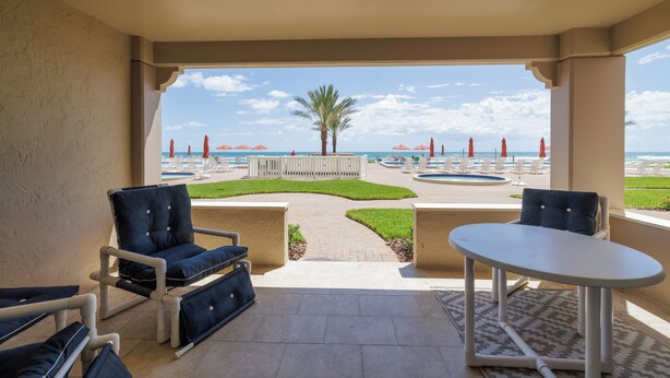 A covered outdoor seating area with a view of a pool and beach umbrellas.