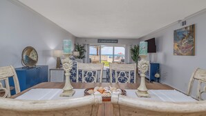 A dining area with a view of the beach, a sign reading 'EAT.BEACH.SLEEP.REPEAT.', and a table set with a basket of fruits.
