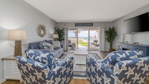 A living room with a sofa, two armchairs, a coffee table, a TV, and a view of the outdoors.