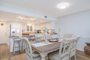 Une cuisine avec des meubles blancs, un îlot central et un coin repas comprenant une table en bois et des chaises blanches.