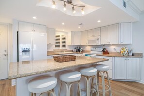A modern kitchen with white cabinetry, a granite countertop, and a built-in island with bar stools.