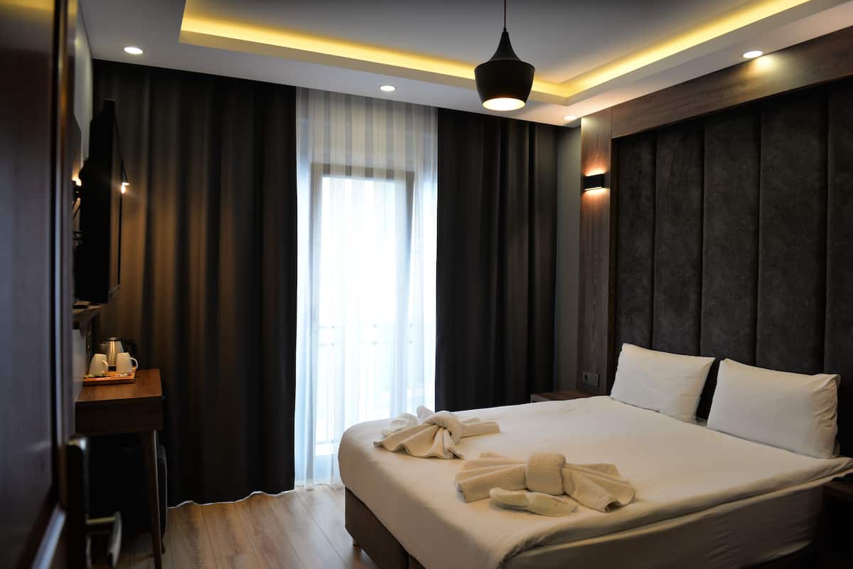 A hotel room with a large bed, a desk with a coffee maker, and a view of the outdoors through a window with curtains.