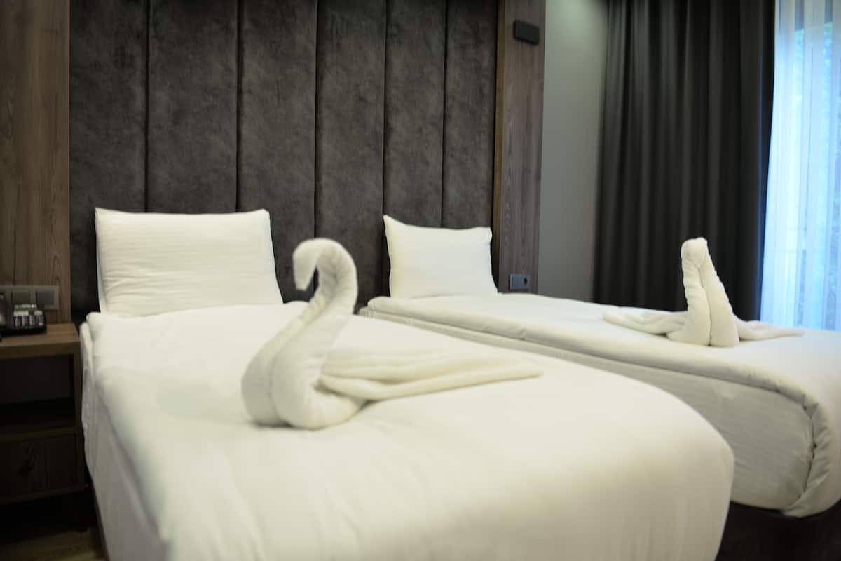 A hotel room with two beds, each with white linens and a swan-shaped towel.