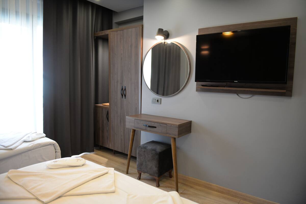 A modern hotel room with a bed, a bedside table, a mirror, a TV, and a wardrobe.