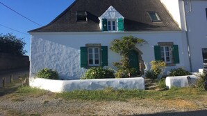 A white building with green shutters, a sloped roof, and a small garden area with bushes and a tree. - Maison de Pêcheur, Port de Penerf. One of a kind! (Damgan)