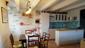 A dining area with a table and chairs, a kitchen with white cabinets and a green backsplash, and a hanging light fixture. - Maison de Pêcheur, Port de Penerf. One of a kind! (Damgan)