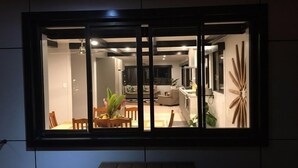 A modern interior with a dining area, kitchen, and living space visible through a large window. - Nevaeh Holiday Home + Pool + Unlimited Internet (Tupapa)