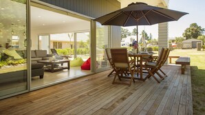 An outdoor patio with a wooden deck, a round table with chairs, and a large umbrella.