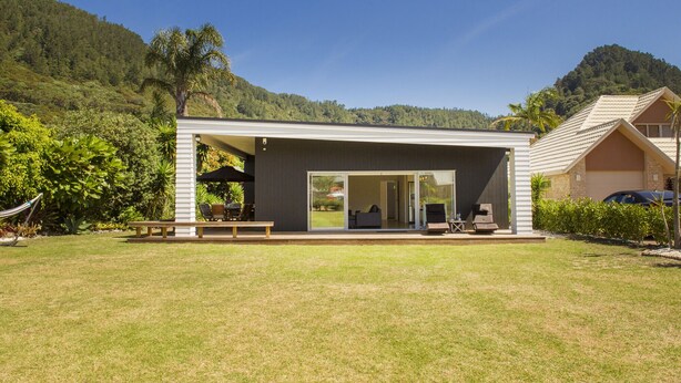 A modern house with a large patio, a dining area, and a view of the surrounding forest.