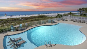 Une piscine dotée de chaises longues, offrant une vue sur la plage et l’océan au coucher du soleil.