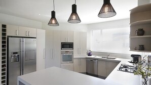 Una cocina moderna con electrodomésticos de acero inoxidable, una encimera blanca e iluminación colgante.