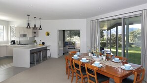 Una cocina moderna con una isla central, un comedor con una mesa grande para seis personas y vistas a un jardín exuberante a través de amplios ventanales.