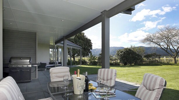 Un patio al aire libre con una mesa de vidrio, sillas a rayas, una parrilla y vistas al paisaje.