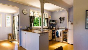 A compact kitchen with a central island, a microwave, a stove, and a refrigerator. - Moa Bach - Blackpool Holiday Home (Oneroa)