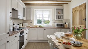 Een keuken met witte kasten, een houten aanrecht, een spoelbak en een magnetron, en een eethoek met een tafel gedekt voor twee personen.