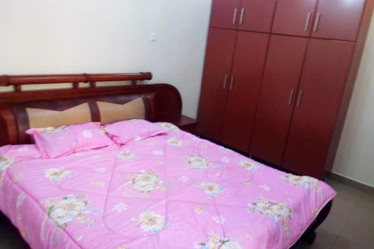 A bedroom with a bed covered in a floral-patterned pink bedspread, a wooden headboard, and a red wardrobe with multiple doors.