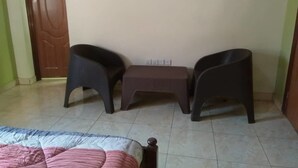 A room with a bed, two chairs, a small table, and a door. - Belize Motel (Kigali)