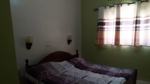 A bedroom with a wooden bed, two wall-mounted light fixtures, and a window with striped curtains. - Belize Motel (Kigali)
