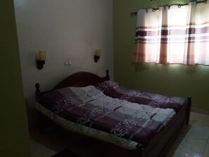 A bedroom with a wooden bed, two wall-mounted light fixtures, and a window with striped curtains. - Belize Motel (Kigali)