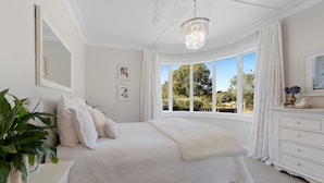 A bedroom with a large bed, a dresser, a mirror, and a window with a view of trees.