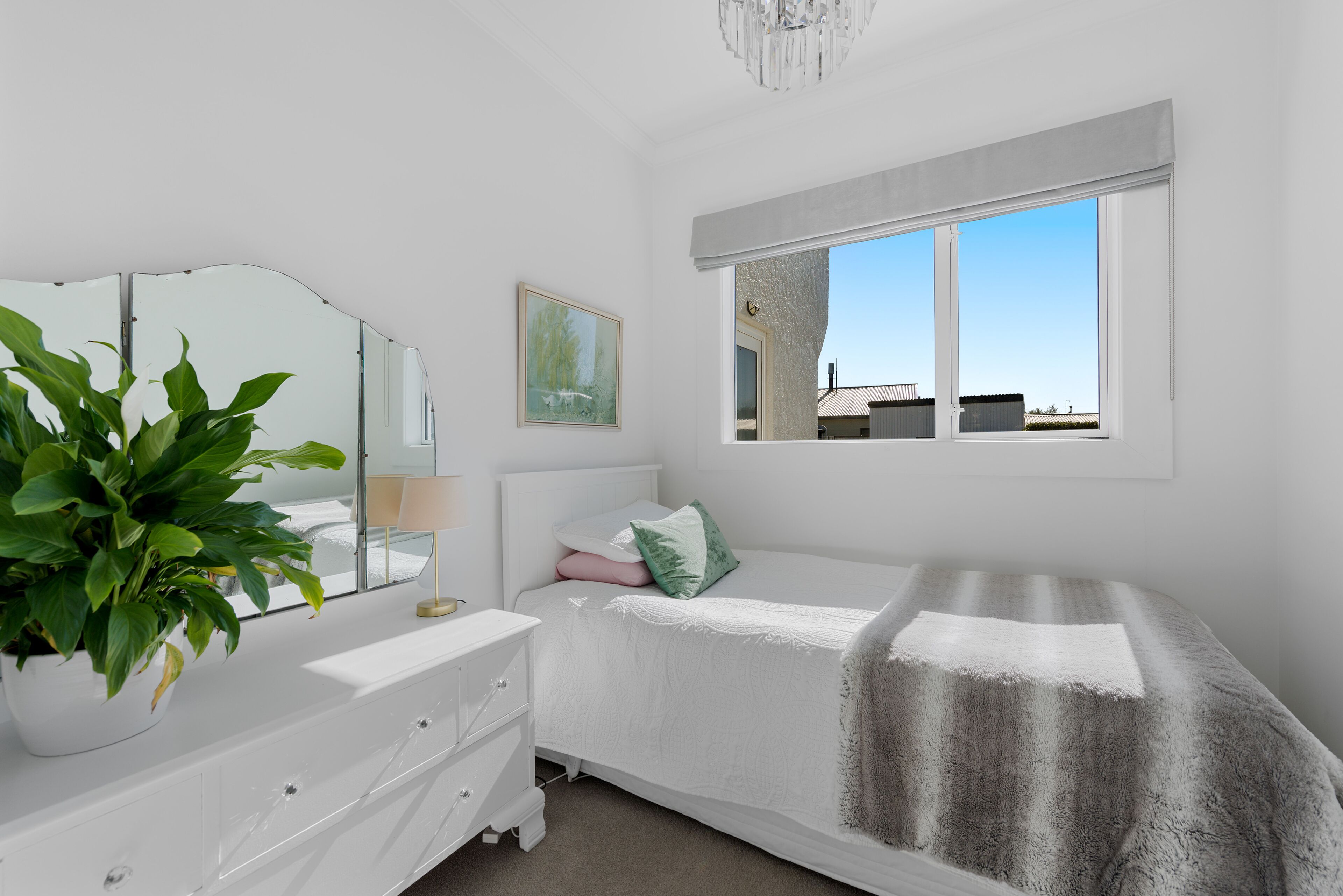 Une chambre à coucher avec un lit, une commode, un miroir, une fenêtre et une plante.