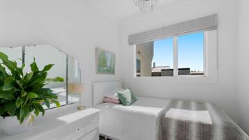 Une chambre à coucher avec un lit, une commode, un miroir, une fenêtre et une plante.