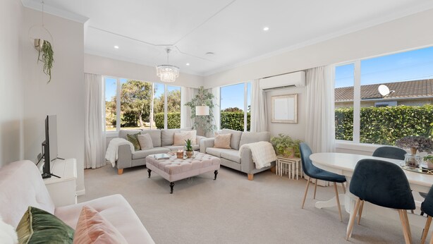 A spacious living room with a large window, a chandelier, and a dining area with a table and chairs.