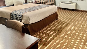 Habitación de hotel con una cama grande, un escritorio, una silla, una ventana con cortinas y un equipo de aire acondicionado.