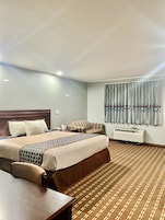 Habitación de hotel con una cama grande, un escritorio, una silla, una ventana con cortinas y un equipo de aire acondicionado.