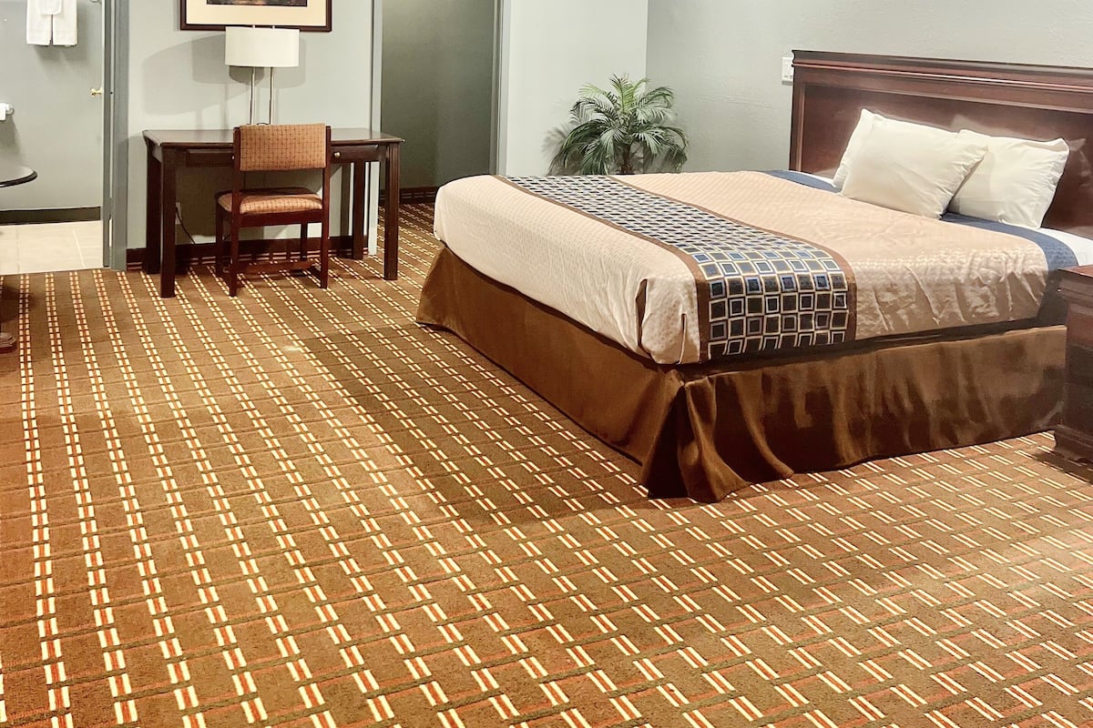 A hotel room with a bed, a desk, a chair, a lamp, and a door.