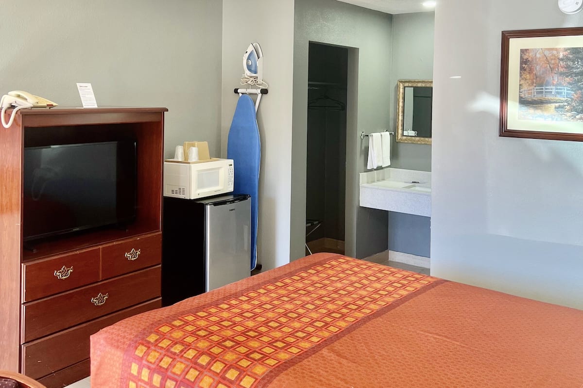A hotel room with a bed, a TV, a desk, a microwave, and a mirror.