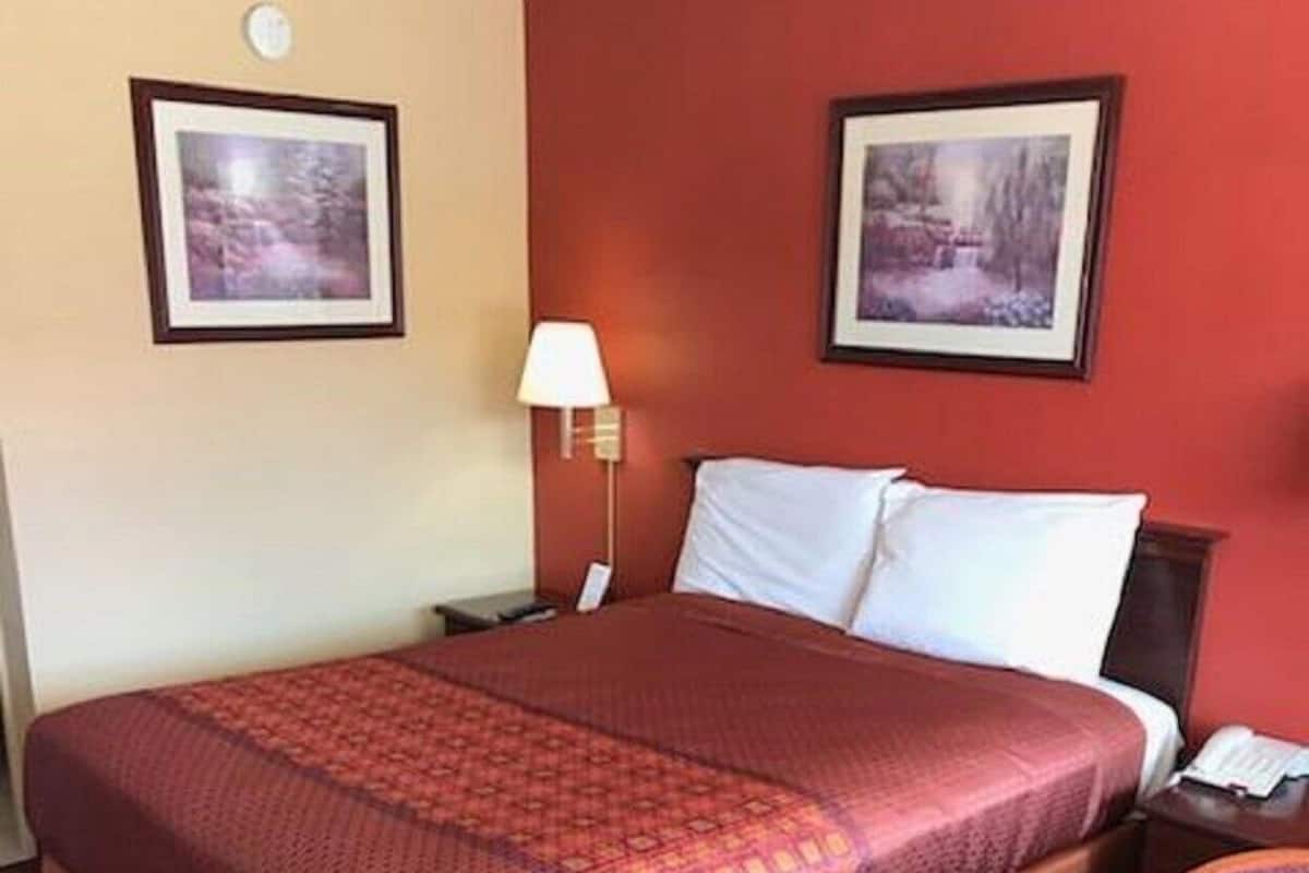 A hotel room with a large bed, a nightstand, a lamp, a chair, and two framed pictures on the wall.