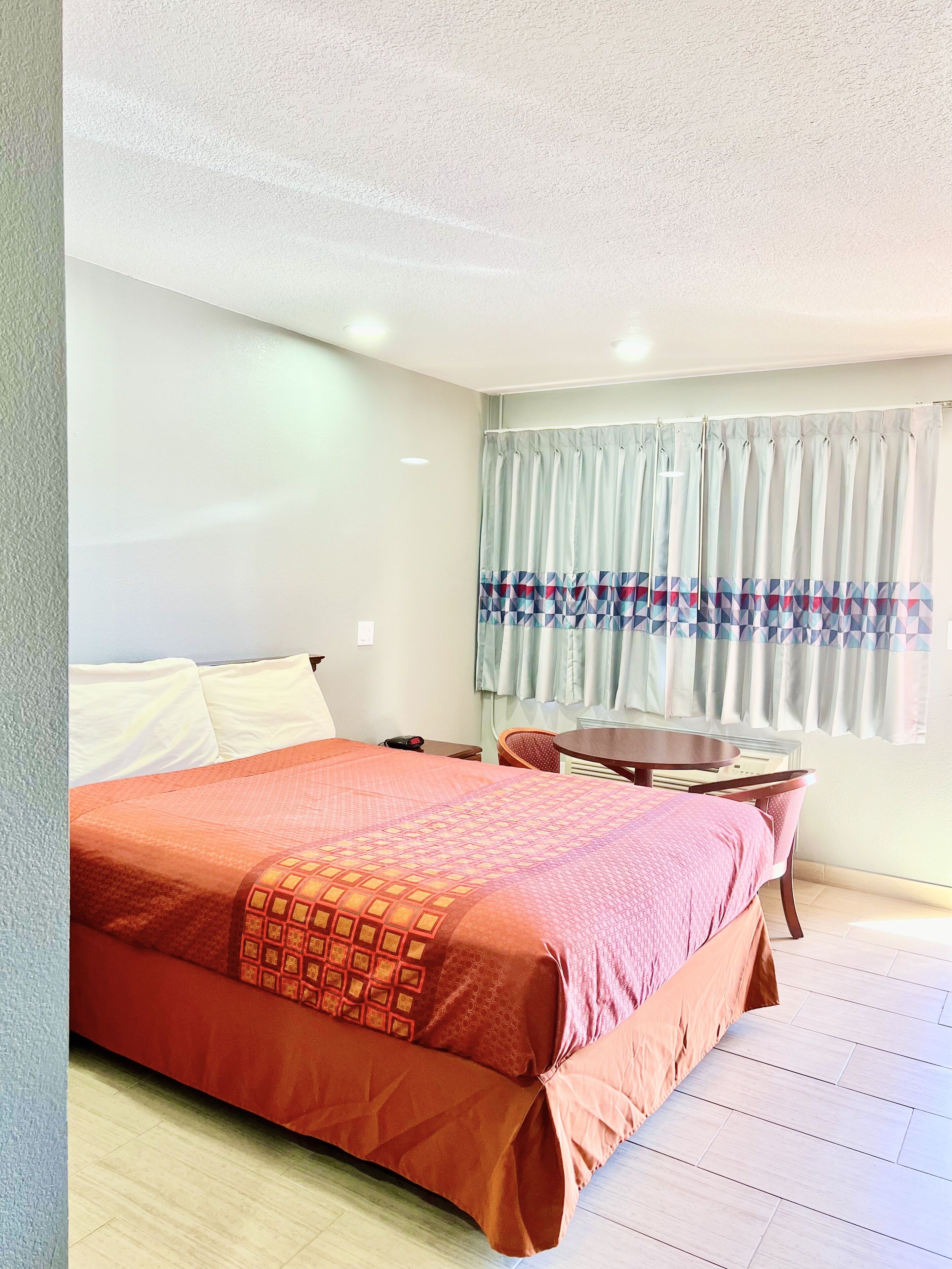 Een hotelkamer met een groot bed, een klein tafeltje en een raam met gordijnen.