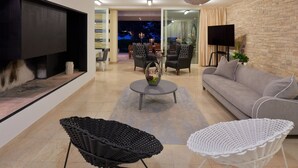 Uma sala de estar moderna com um sofá, uma mesa de centro e duas poltronas. Há uma TV na parede, uma lareira e uma parede de pedra.