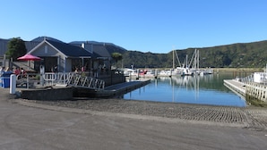 Un port de plaisance avec des bateaux amarrés, un bâtiment doté d’une zone abritée et, au loin, un paysage vallonné.