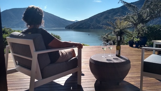 Une personne assise sur une chaise longue, face à un lac, avec des montagnes en arrière-plan.