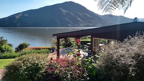 Une vue sur le lac, avec une montagne en arrière-plan, un espace extérieur aménagé et abrité, et une végétation luxuriante.
