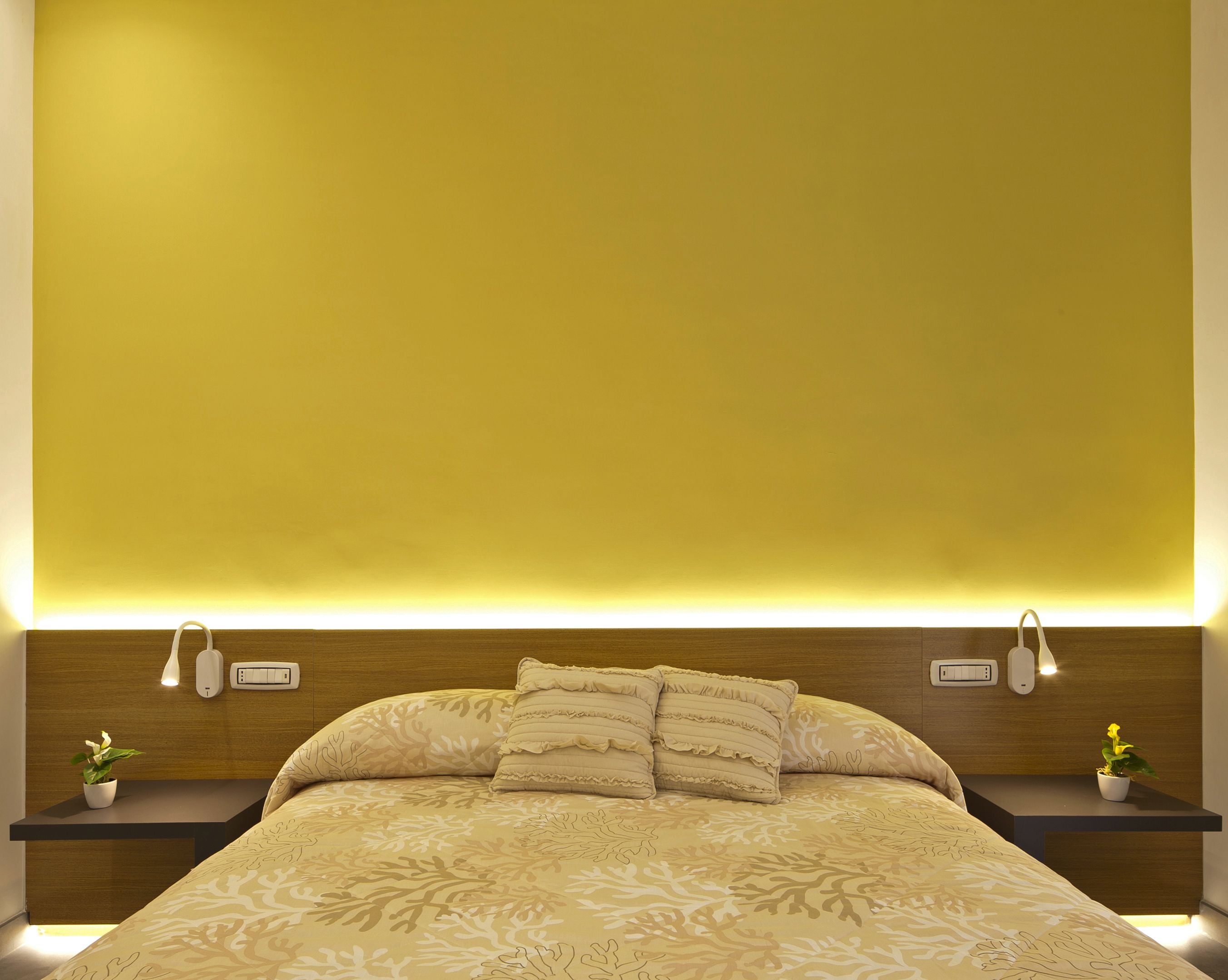 A neatly made bed with a patterned bedspread, two bedside tables with lamps, and a wall-mounted light fixture above the bed.