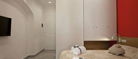 A modern hotel room with a bed, a TV, a wardrobe, and an air conditioning unit.