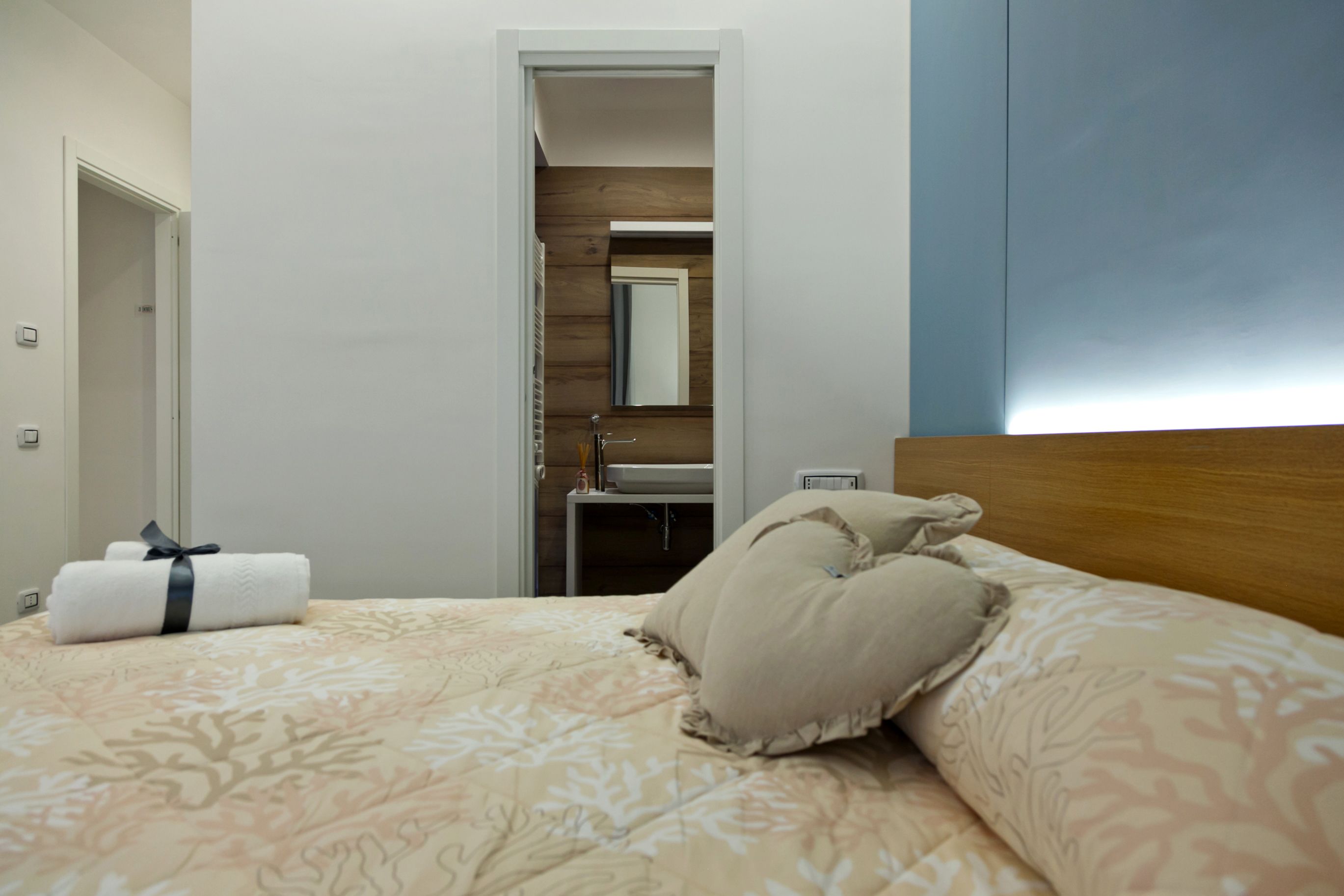 A hotel room with a bed, a bathroom with a mirror, and a wooden headboard.