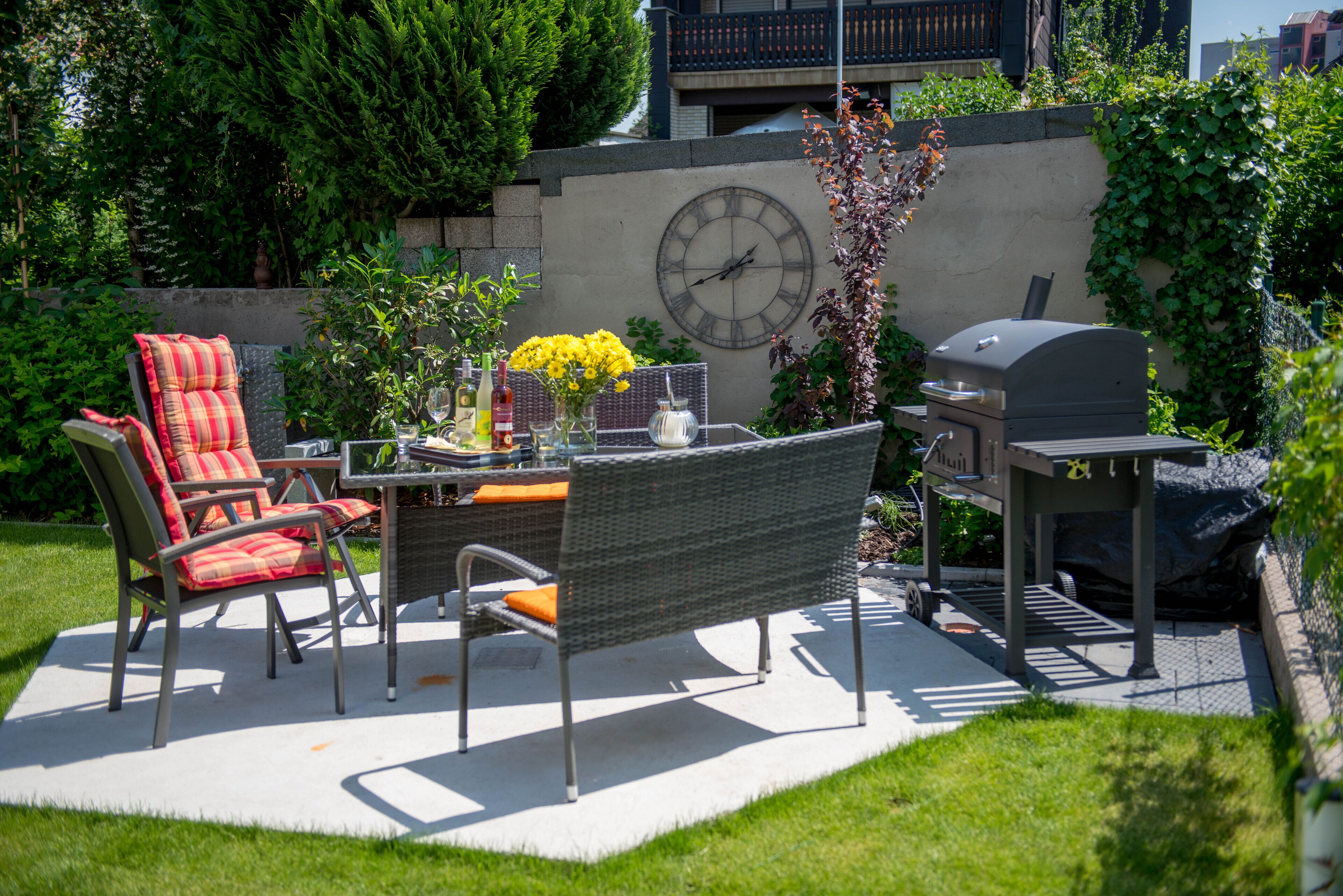 Une terrasse extérieure équipée d’un ensemble de mobilier de jardin, de chaises, d’une horloge et d’un barbecue.