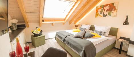 A bedroom with a skylight, a bed with pillows, a bedside table, and a chair.