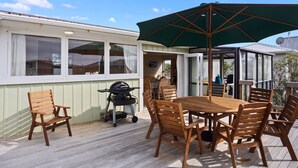 Un espacio de comedor al aire libre techado con mesa, sillas, una parrilla y un paraguas grande.
