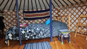 Un llit amb un estovat de punts i ratlles, una escala de fusta i una taula petita amb decoracions colorades en una habitació que sembla una tenda.