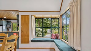 Ein Zimmer mit Holzboden, einer Sitzbank mit Kissen, einem Holzstuhl und einem kleinen Tisch.