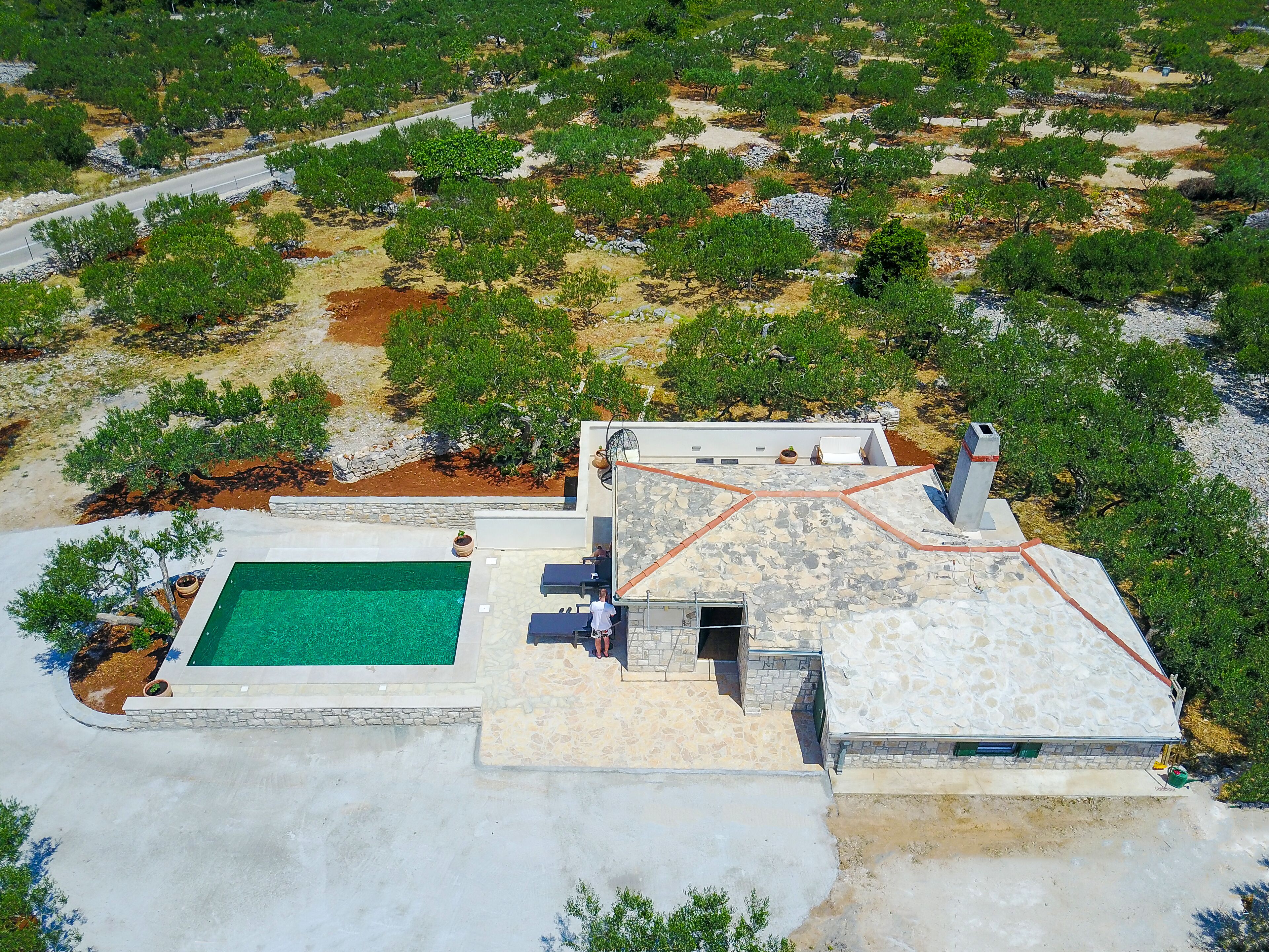 Vue aérienne d’une propriété dotée d’une piscine, d’un espace salon extérieur et d’un toit en pierre.