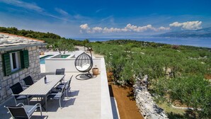Une terrasse extérieure avec une table et des chaises, un fauteuil suspendu et une vue sur la mer et les collines.