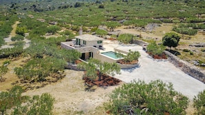Une villa moderne dotée d’une piscine, entourée d’un paysage naturel composé d’arbres et de collines.