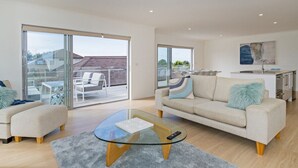 Un salon moderne avec une table basse en verre, un canapé beige et une vue sur un balcon aménagé avec du mobilier d’extérieur.