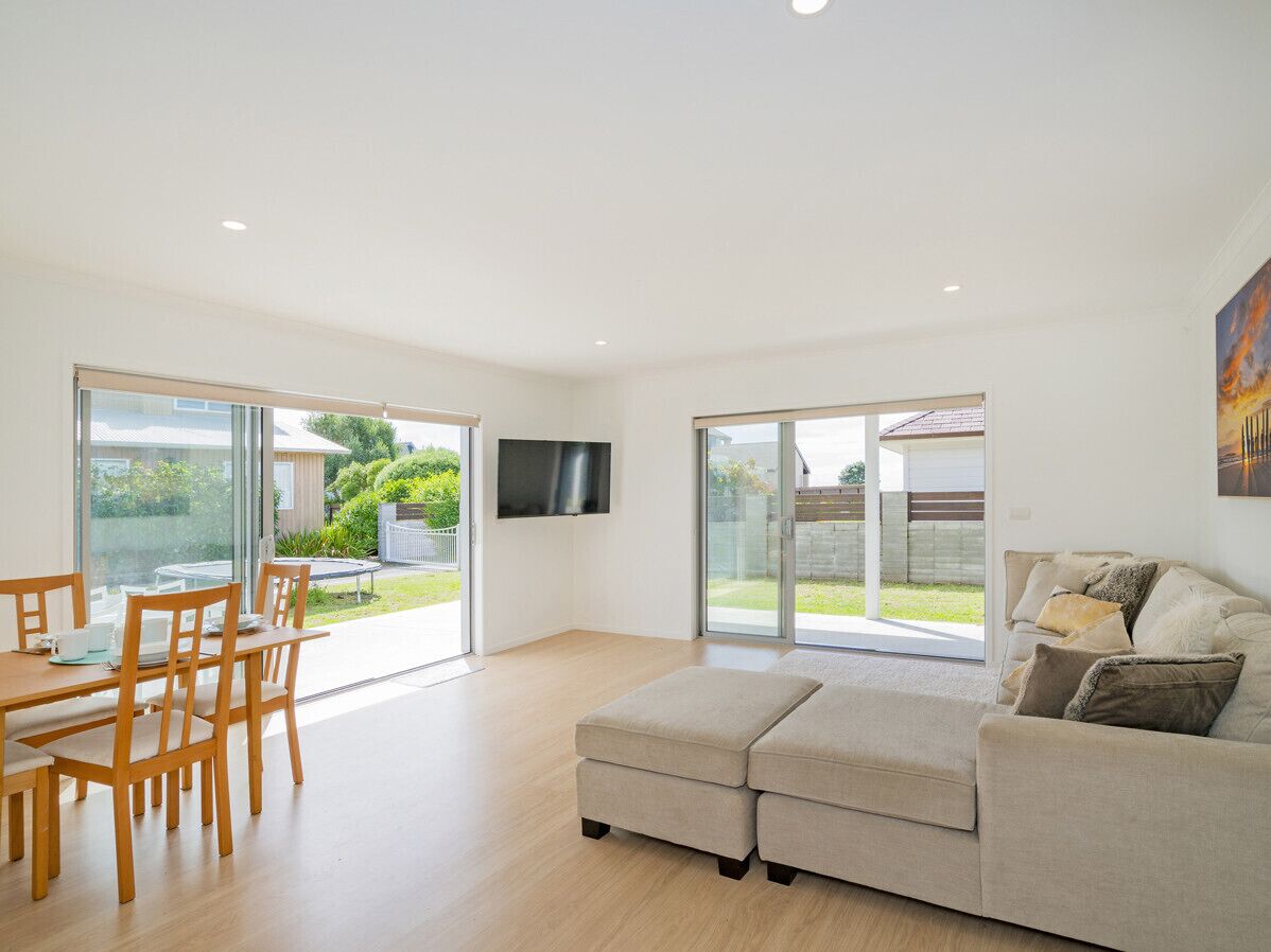 A modern living room with a sofa, a dining table with chairs, and a TV mounted on the wall.